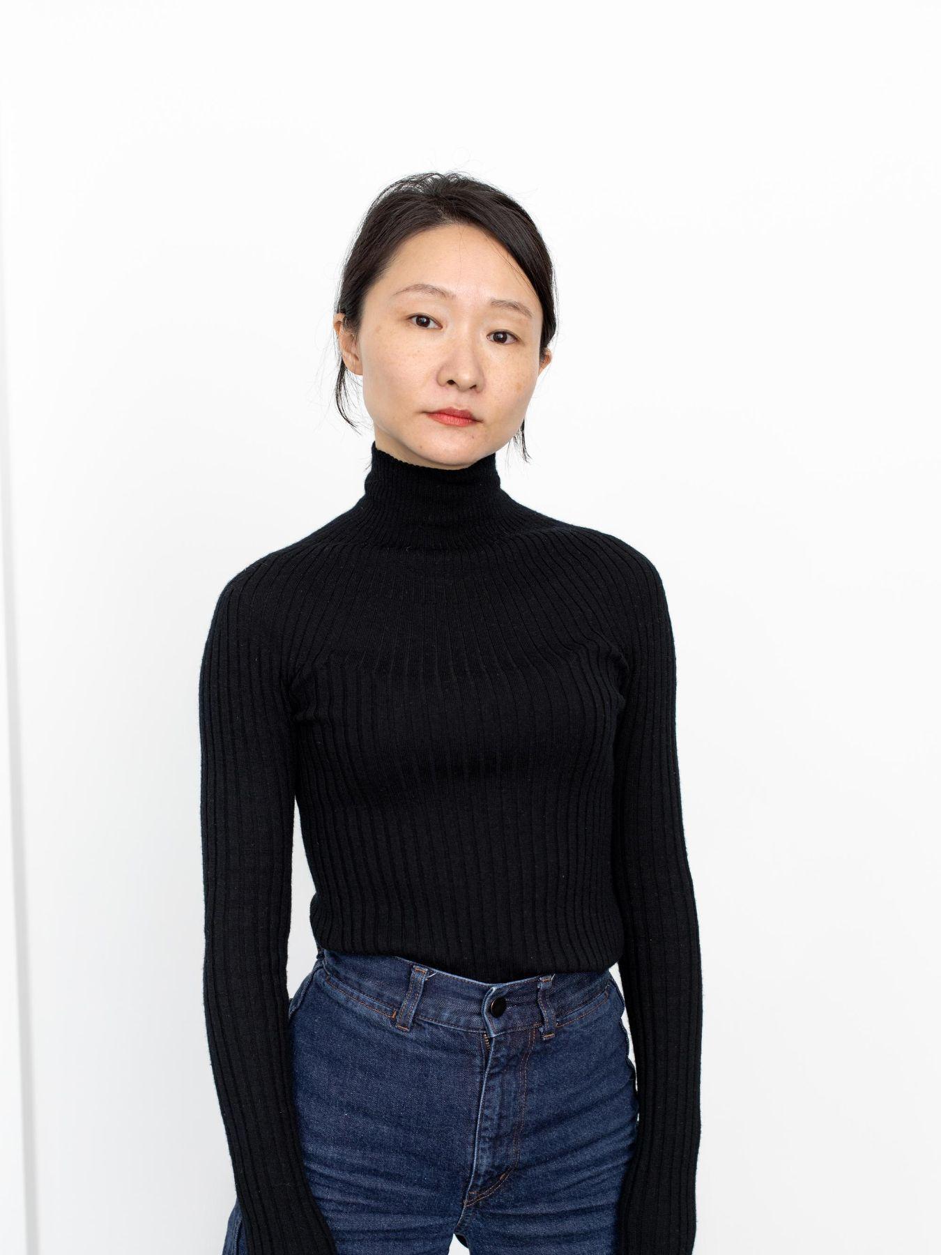 Eine junge Frau in einem schwarzen Rollkragenpulli und Jeans.