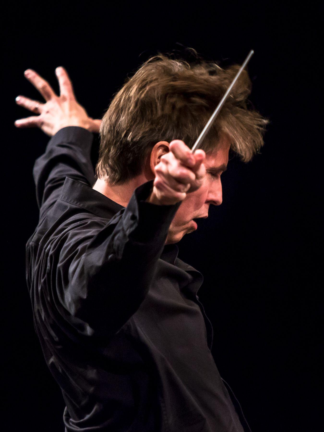 Ein Dirigent, Esa-Pekka Salonen, breitet die Arme vor dem Orchester aus.