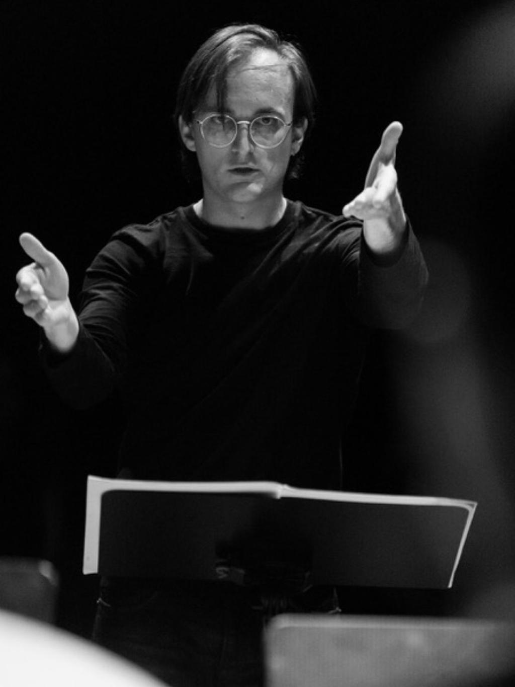 Yannick Mayaud blickt vom Notenpult auf und streckt beide Arme vor sich.