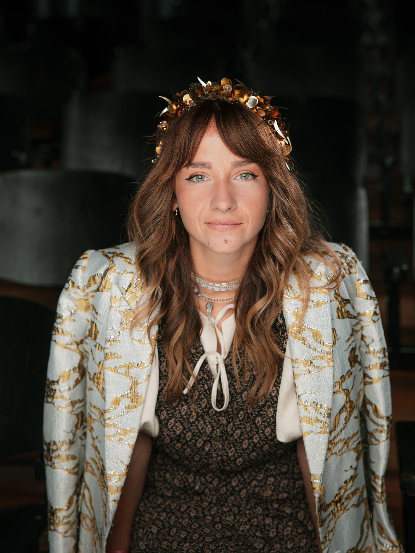 A woman with long brown hair wearing a floral crown and a blue jacket