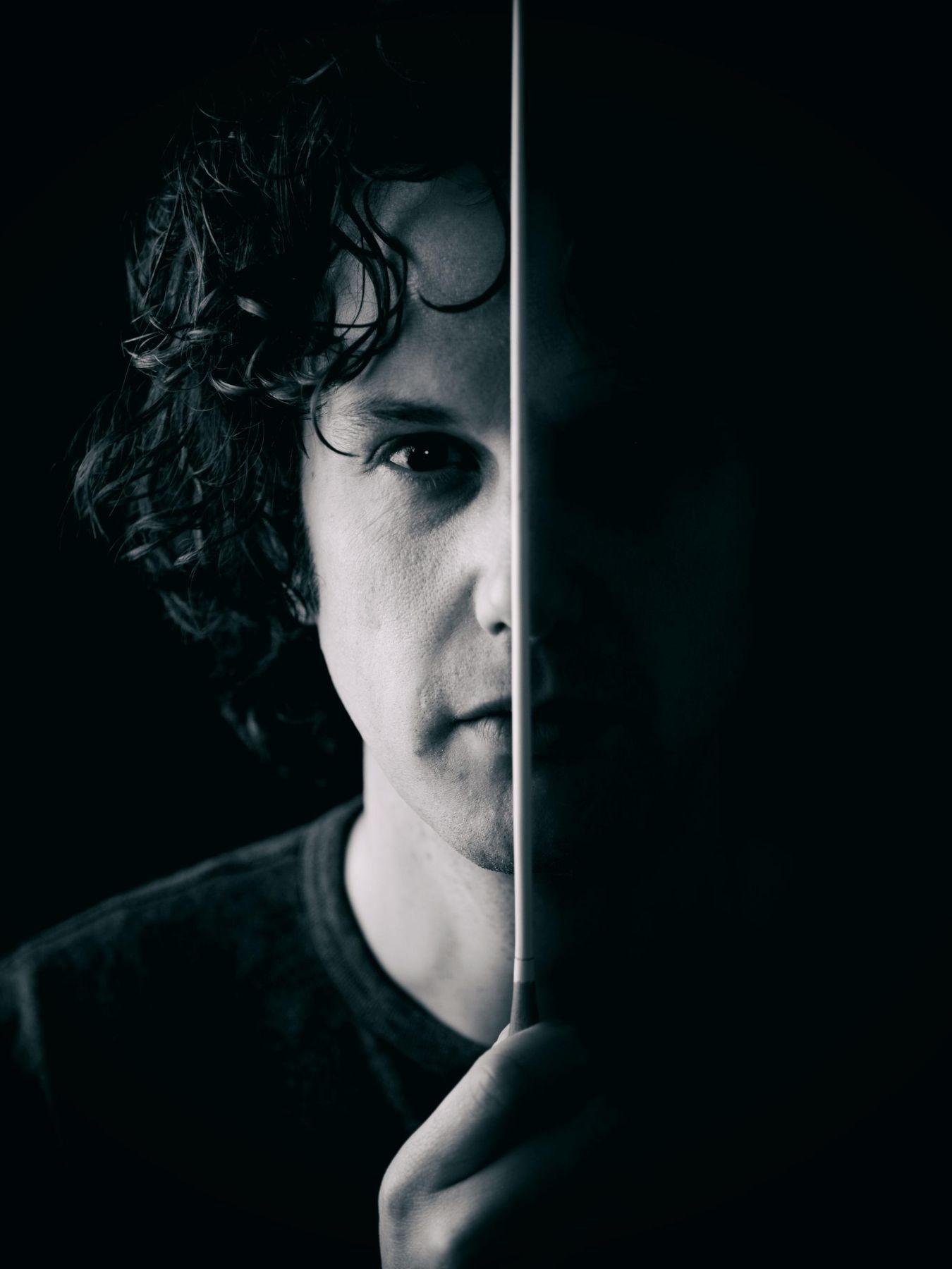 The face of a man looking directly into the camera is shown in black and white. The baton divides his face in two, with the right half being black.