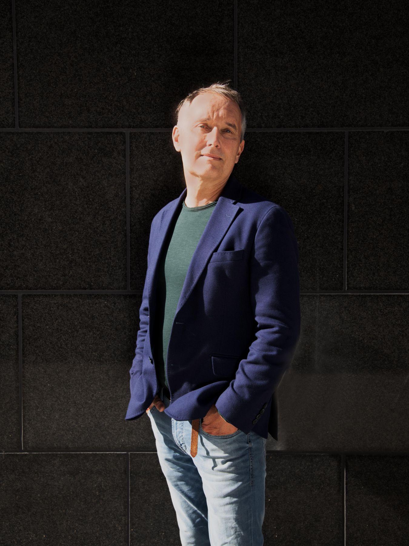 Nagy hat die Hände in den Hosentaschen und trägt ein Sakko.