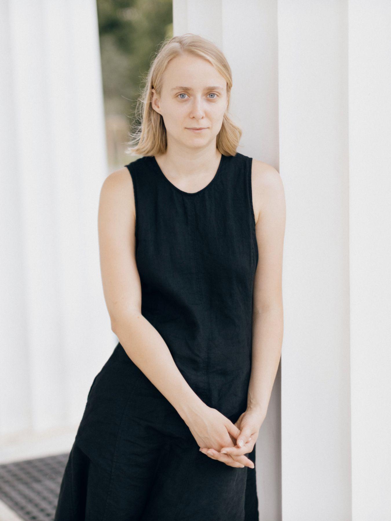 A woman in a black dress stands in front of white columns.