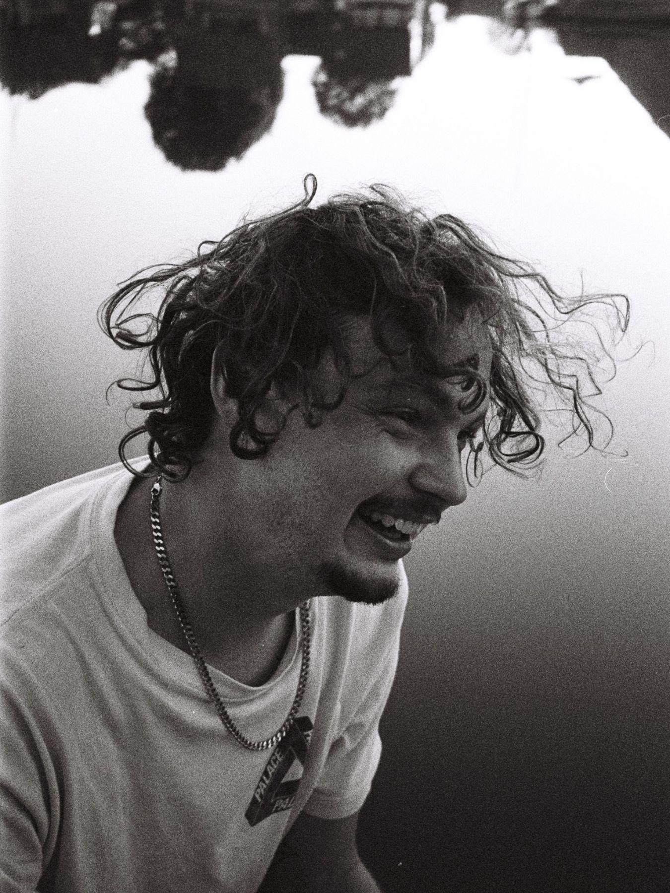 A black and white portrait of Pelle Schilling. He is smiling, his hair flying in motion.