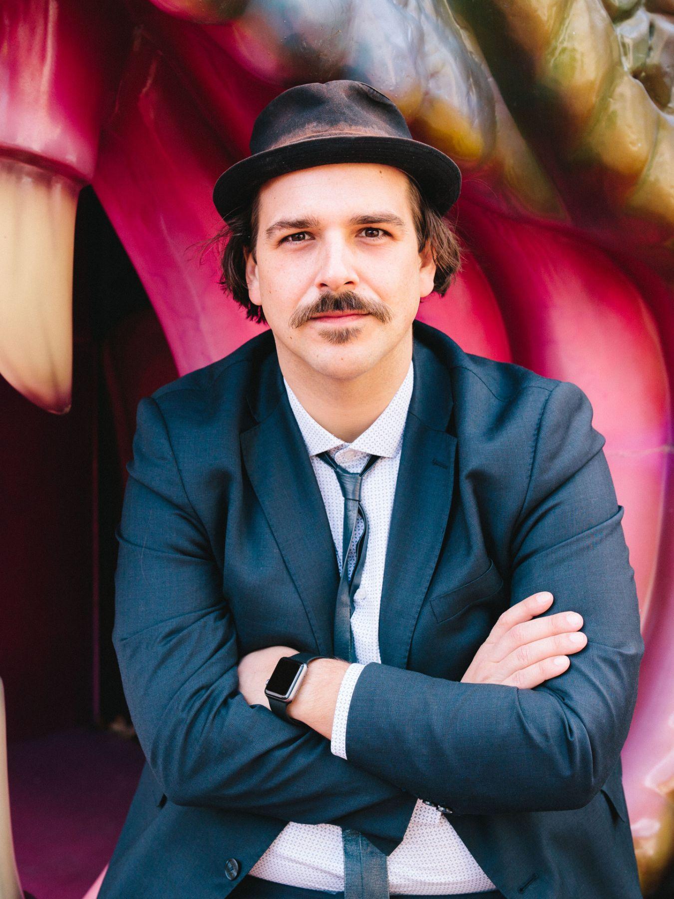 A young man in a suit, with a tie and hat.