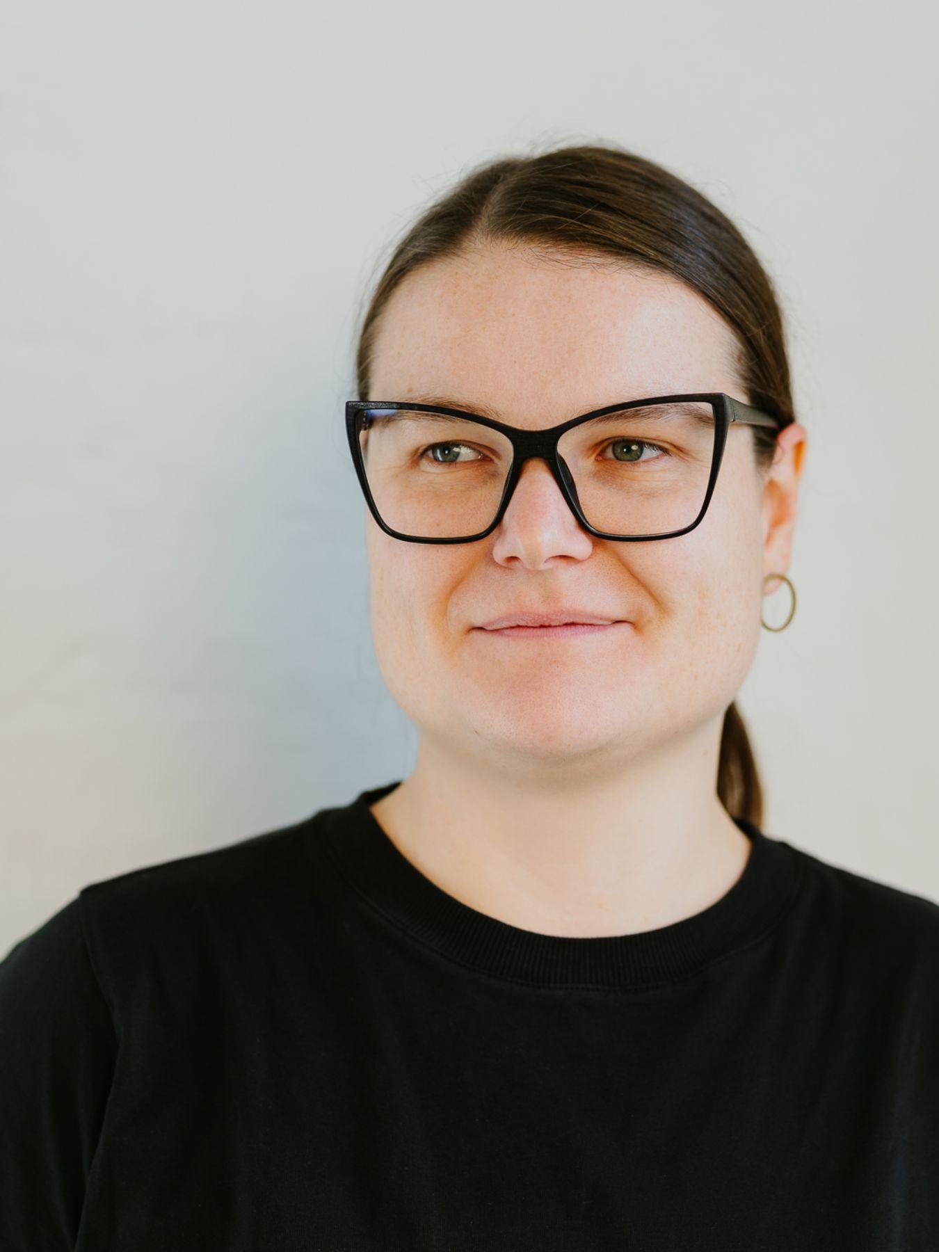 A woman with a ponytail and glasses looking to the left