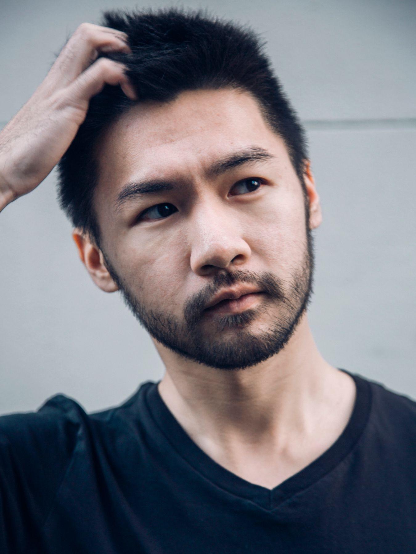 A young man with a beard leans his head on his right hand.