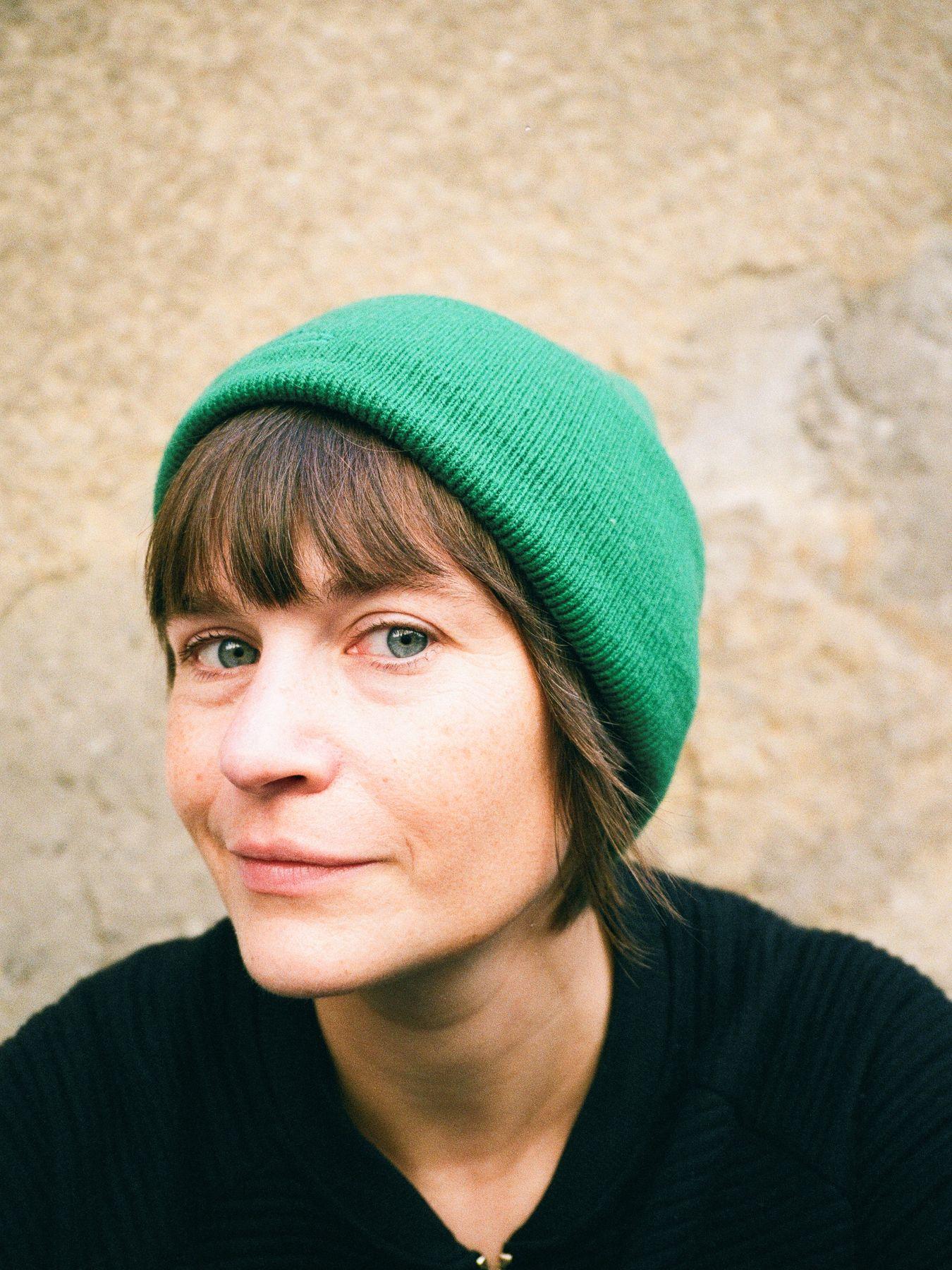 A woman with blue eyes in a green hat and a black jumper.