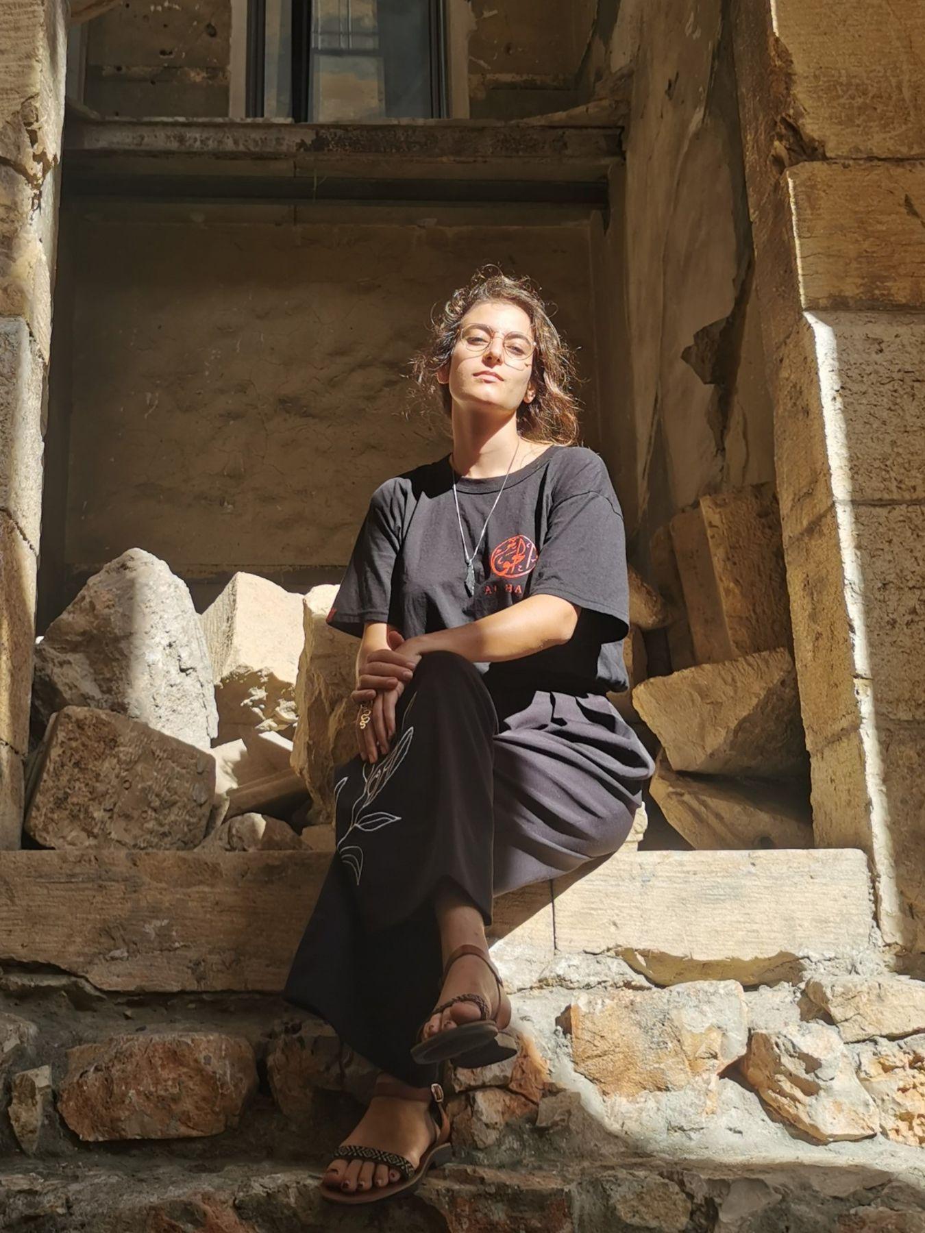 Eine junge Frau mit hellbraunem Haar und Brille in einem schwarzen T-Shirt und einer schwarzen Hose.