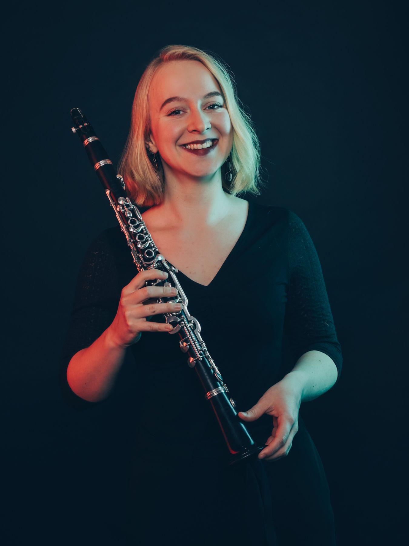 Eine Frau mit schulterlangen blonden Haaren schaut lachend in die Kamera und hält ihre Klarinette in den Händen.