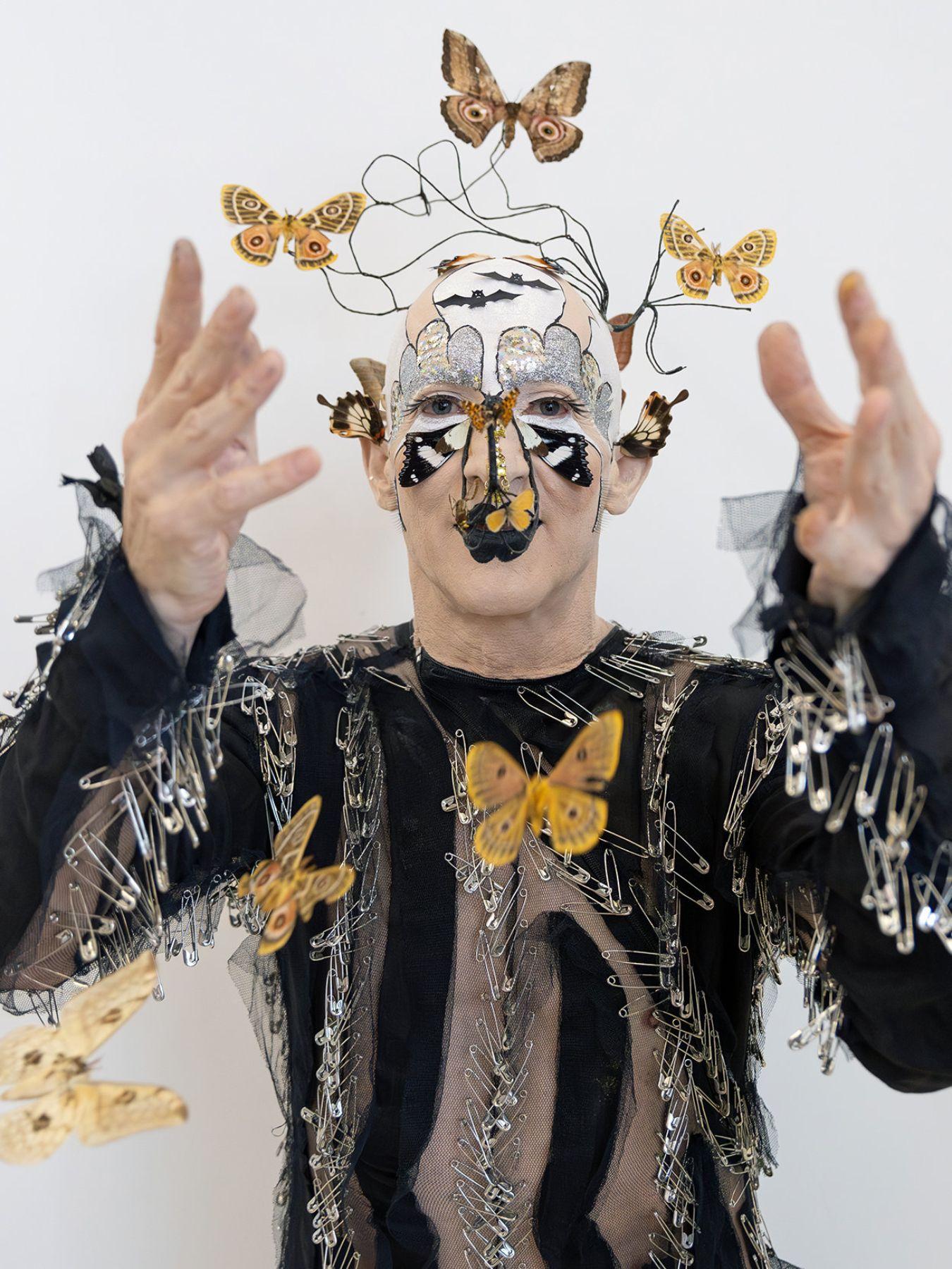 A man in a costume with butterflies, safety pins and black tulle