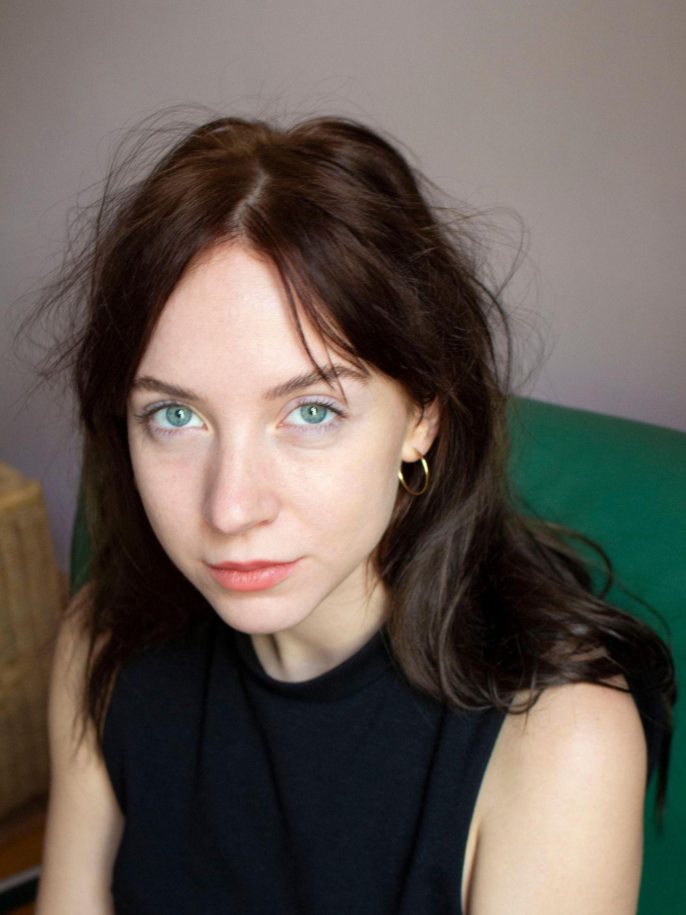 Eine junge Frau mit blauen Augen in einem schwarzen, ärmellosen Oberteil.