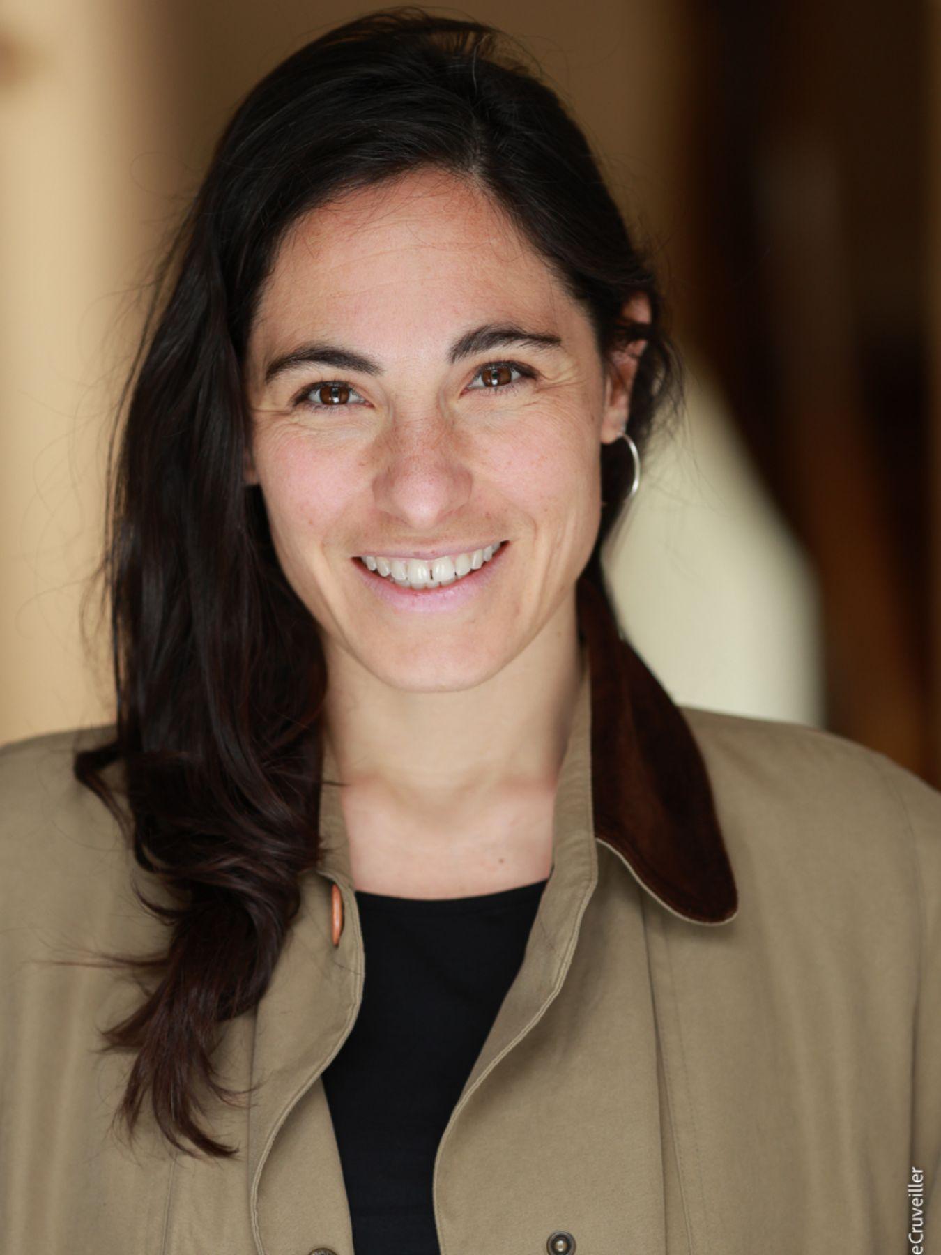 A woman with long dark-brown hair wearing an olive-coloured jacket
