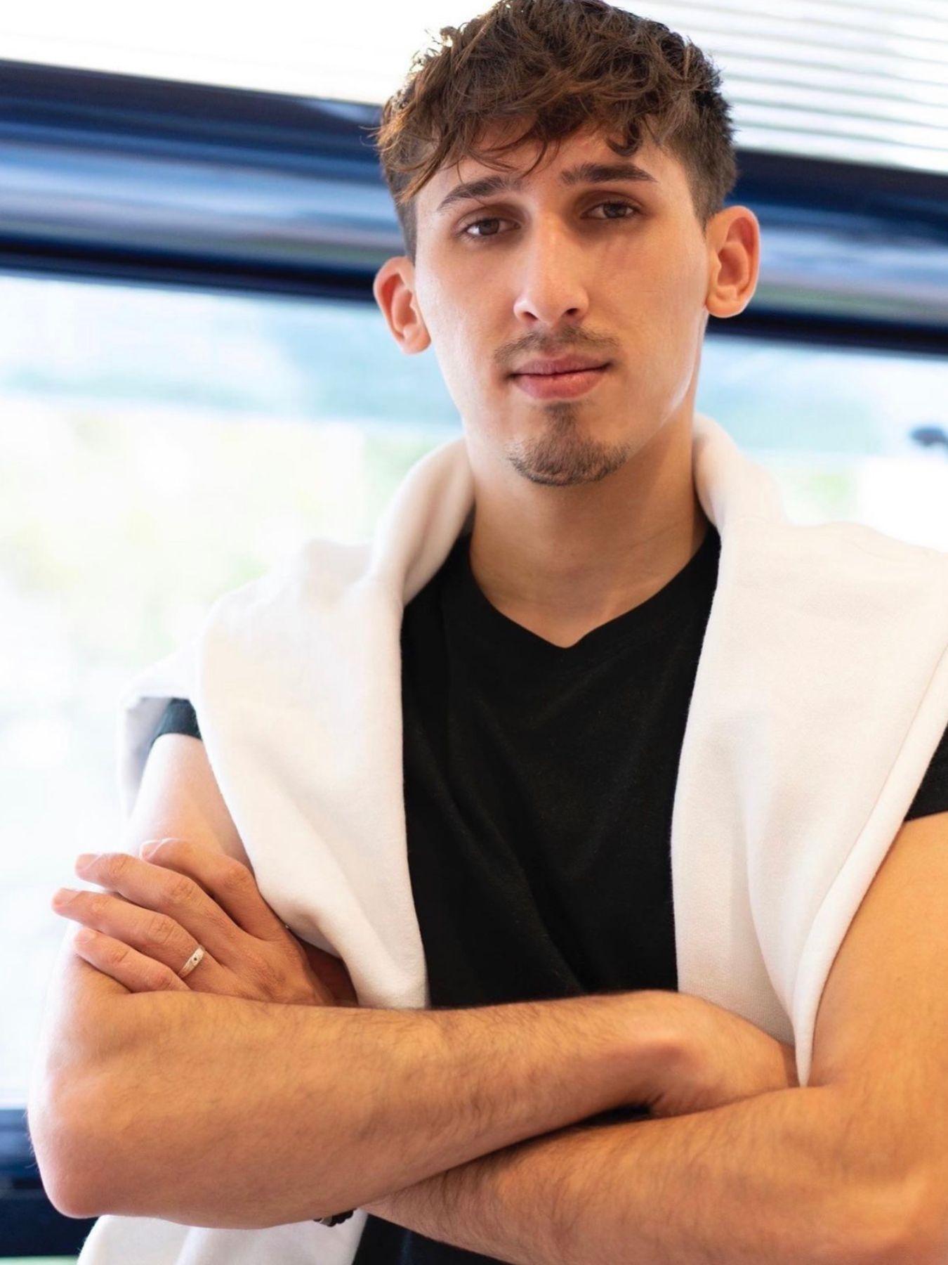 Portrait of a man. He has his arms crossed and is wearing a white jumper over his shoulders.