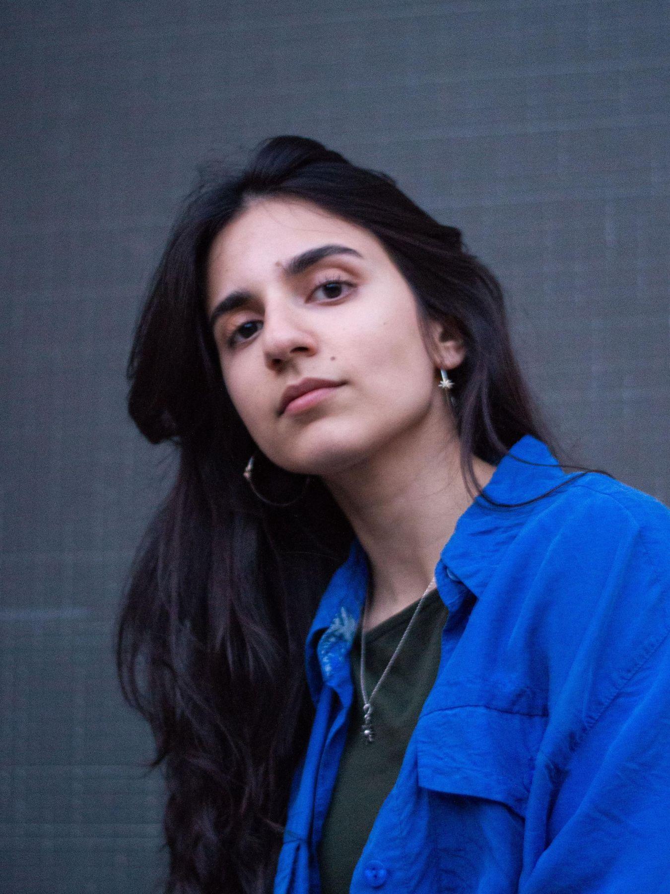 Eine Person mit langem dunkelbraunen Haar und blauem Hemd.