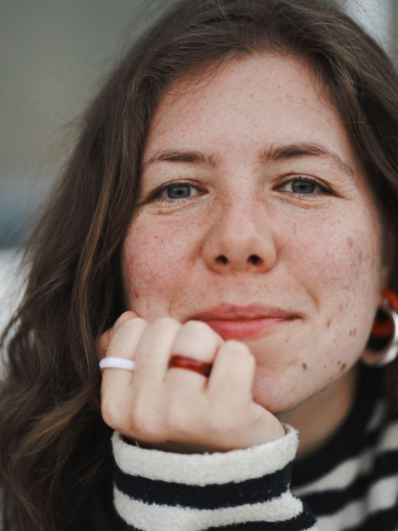 Eine Person mit langem braunem Haar und gestreiftem Pullover.