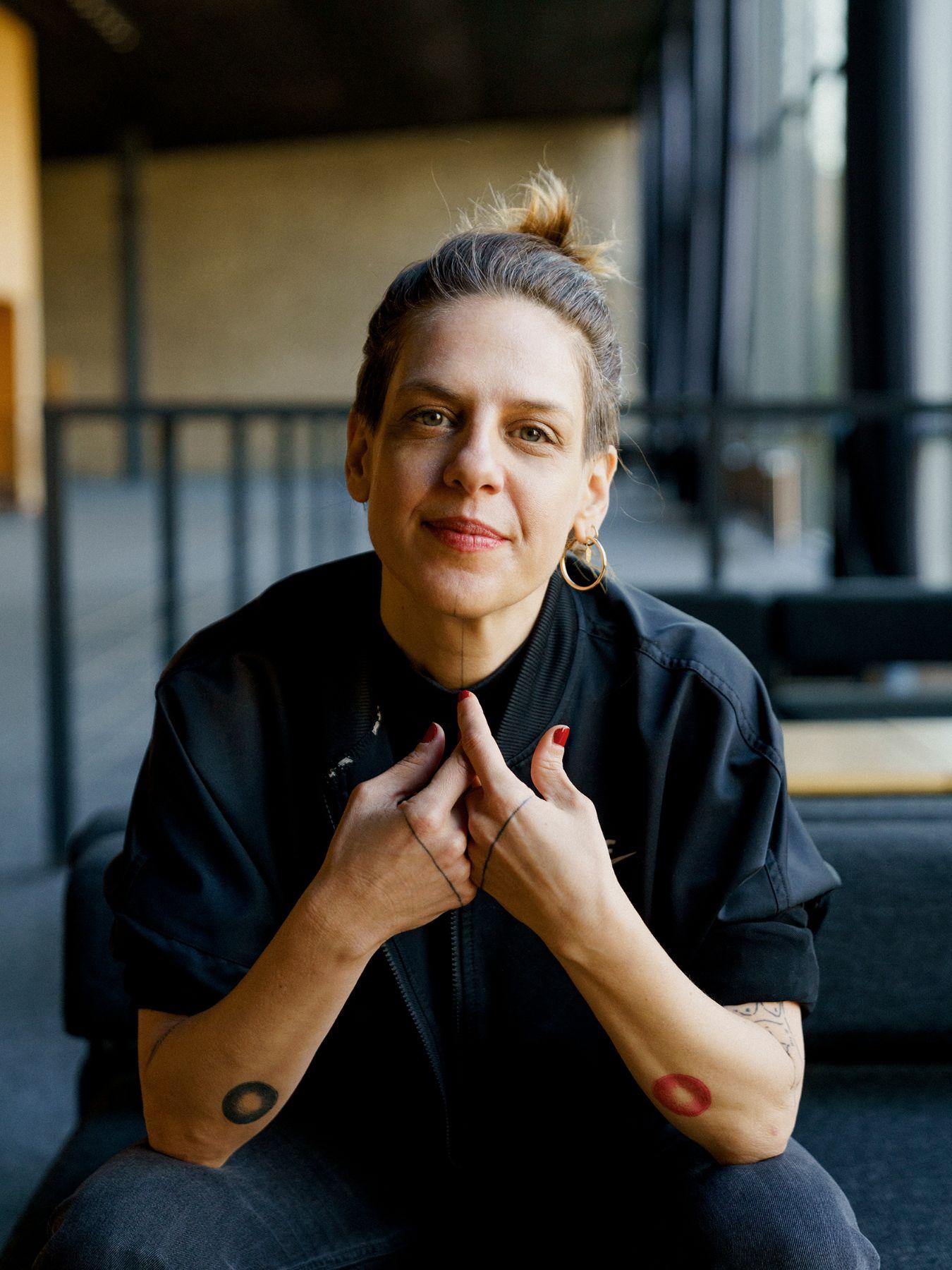 A woman with fair hair, she is wearing a dark blue shirt and a golden earring