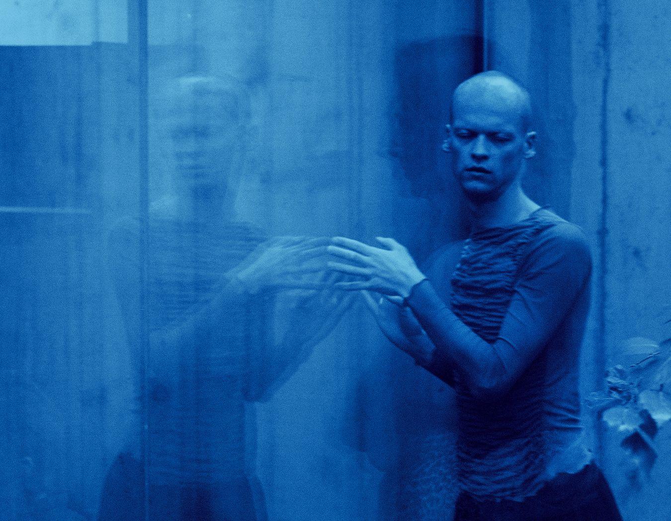 Person bewegt die Hände vor einer spiegelnden Fläche; das Bild ist blau eingefärbt und zeigt eine verschwommene Spiegelung.