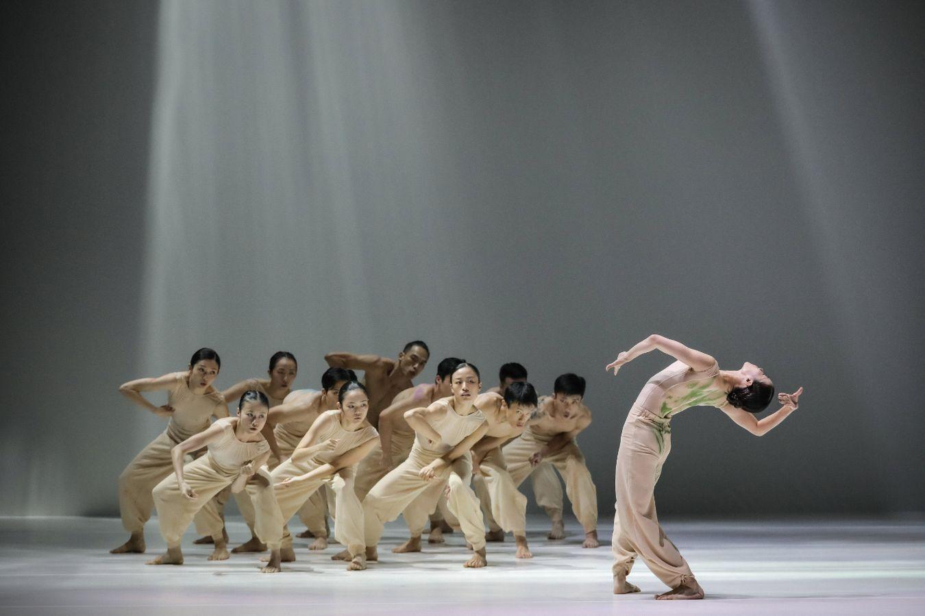 Group of performers moves in unison on a stage, one performer prominently leaning back in front.