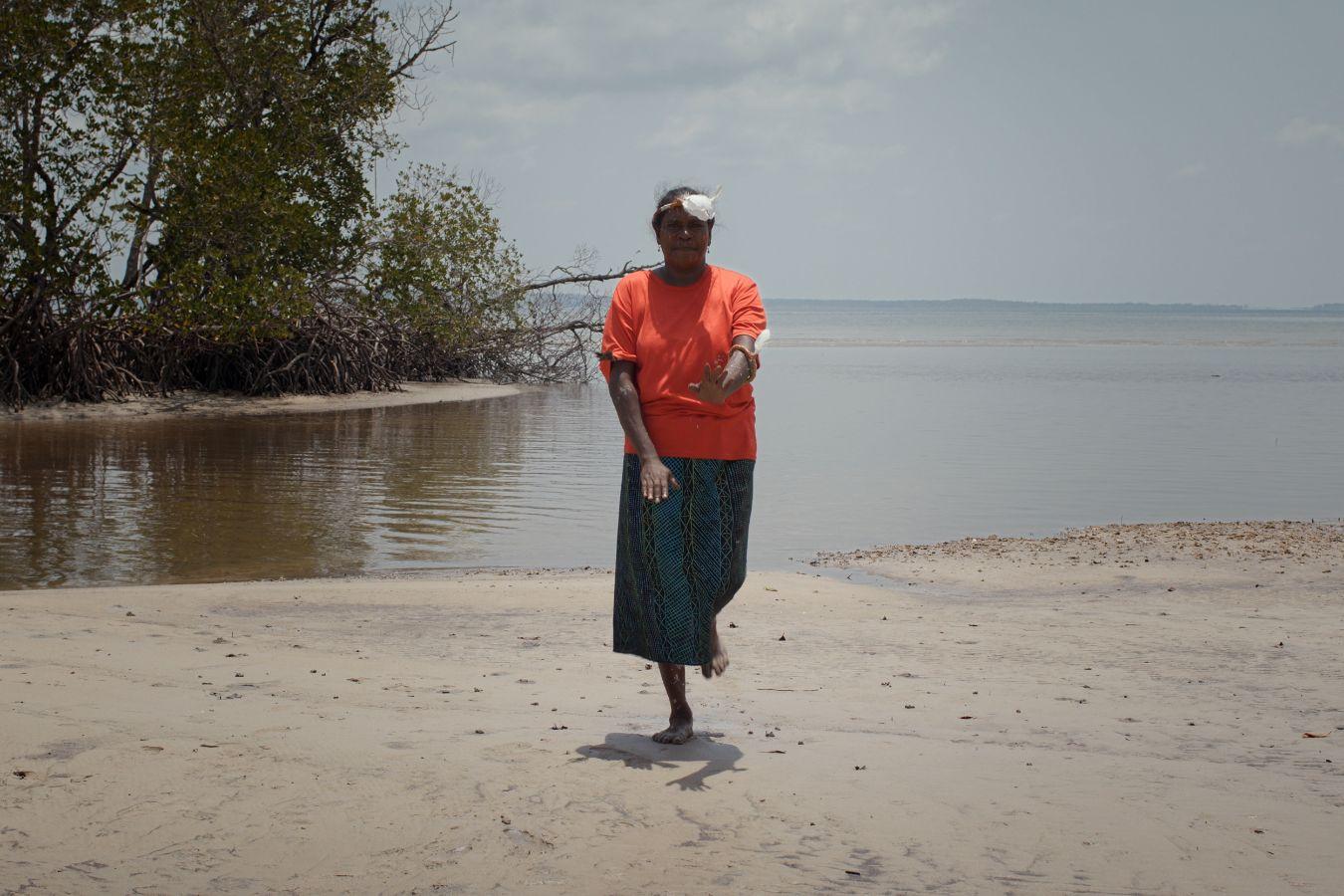 Eine Frau mit bunter Kleidung und Federschmuck tanzt am Strand