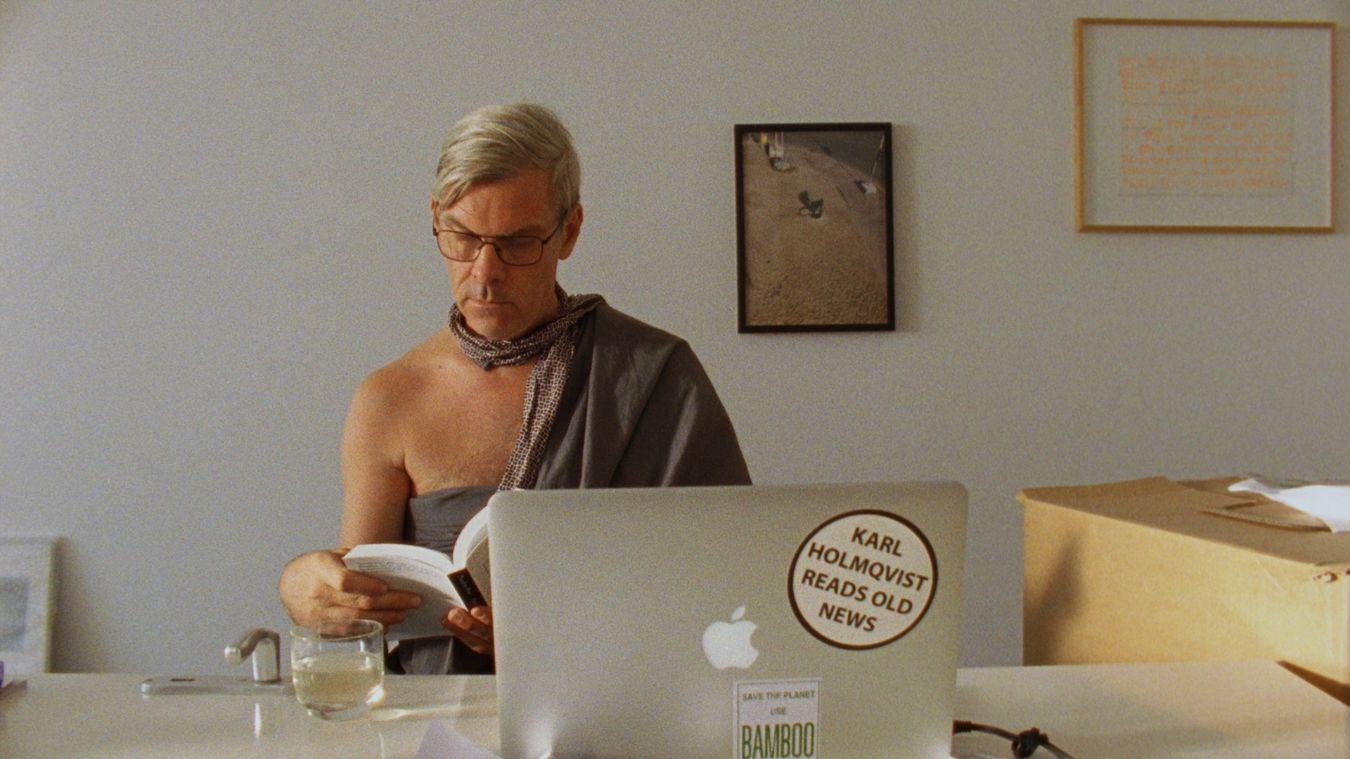 Filmstill aus Rirkrit Tiravanijas "Karl’s Perfect Day", das den Künstler Karl Holmqvist lesend an einem Schreibtisch zeigt.