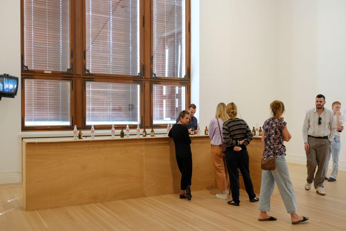 Mehrere Personen stehen an einem Bartresen, auf dem leere Cola- und Bierfalschen stehen.