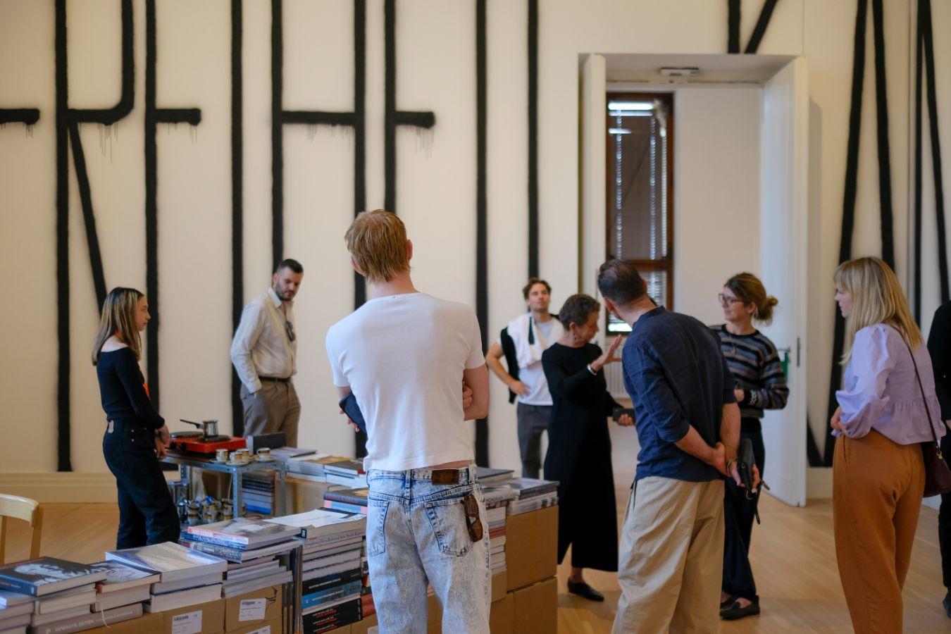 Several people are standing in an exhibition room listening to a guided tour.