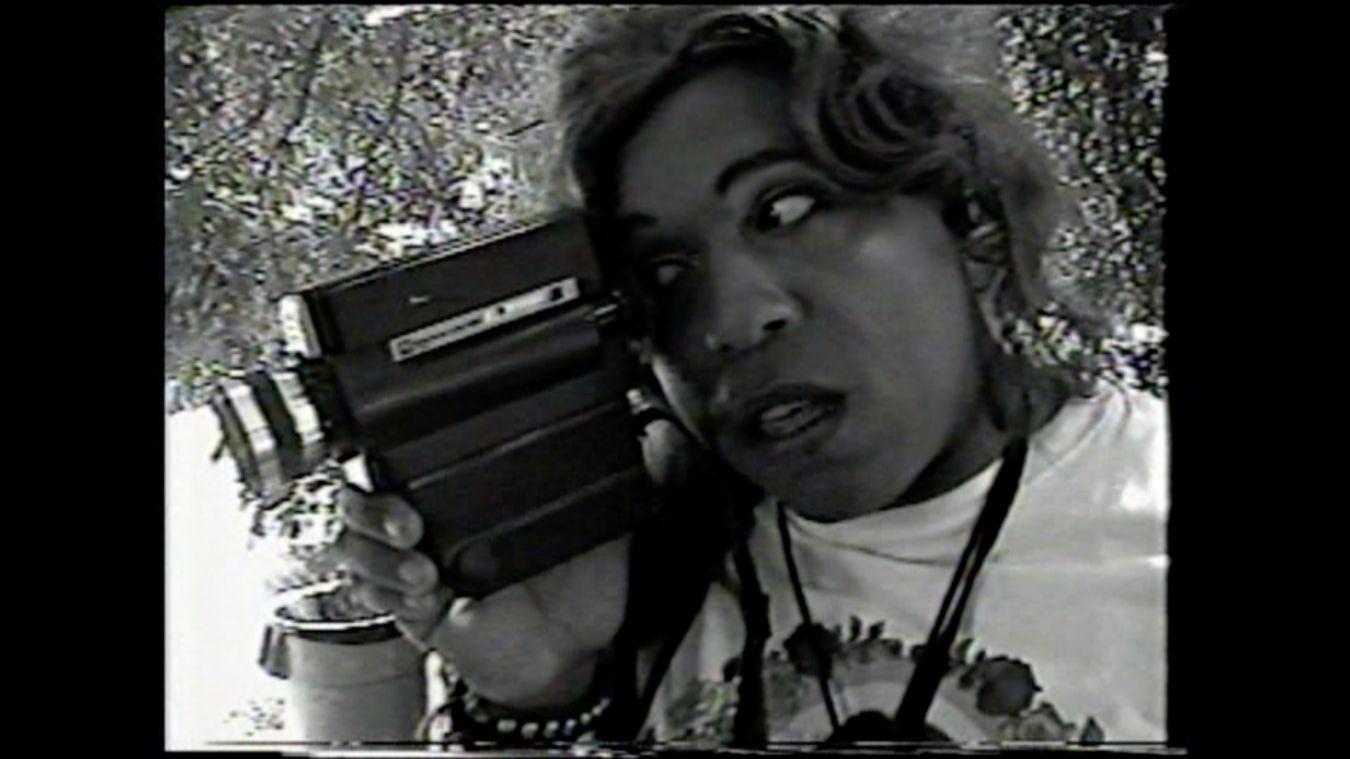 Vaginal Davis hält einen Camcorder in der Hand und schaut in die Linse.