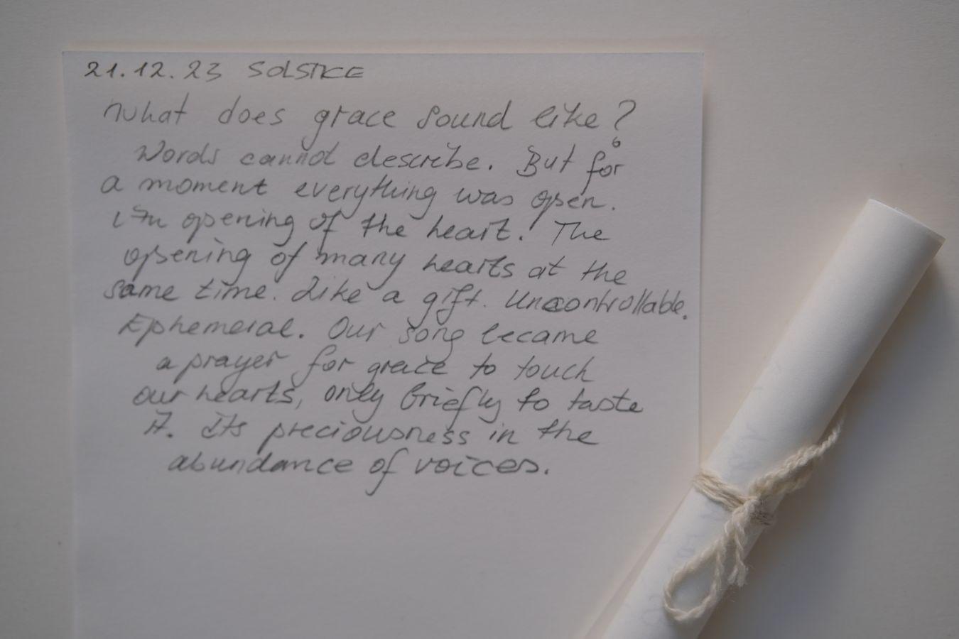 Handschriftlich verfasster Text auf Papier mit Datum 21.12.23 und dem Titel Solstice. Daneben ein gerolltes Papier, mit Schnur gebunden.