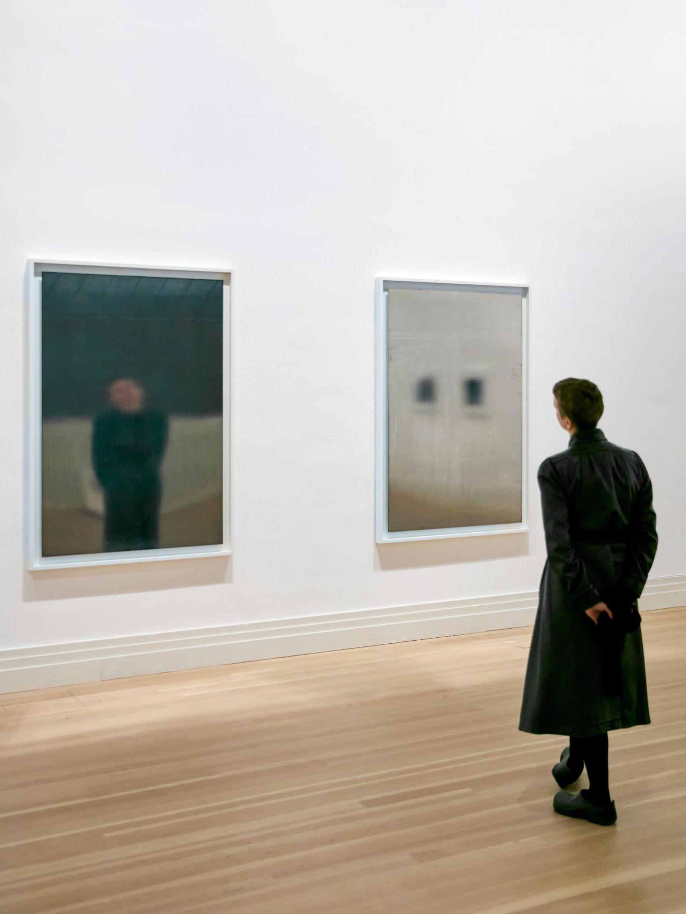 Eine Person, die mit dem Rücken zur Kamera vor zwei rechteckigen, spiegelartigen Kunstwerken steht.