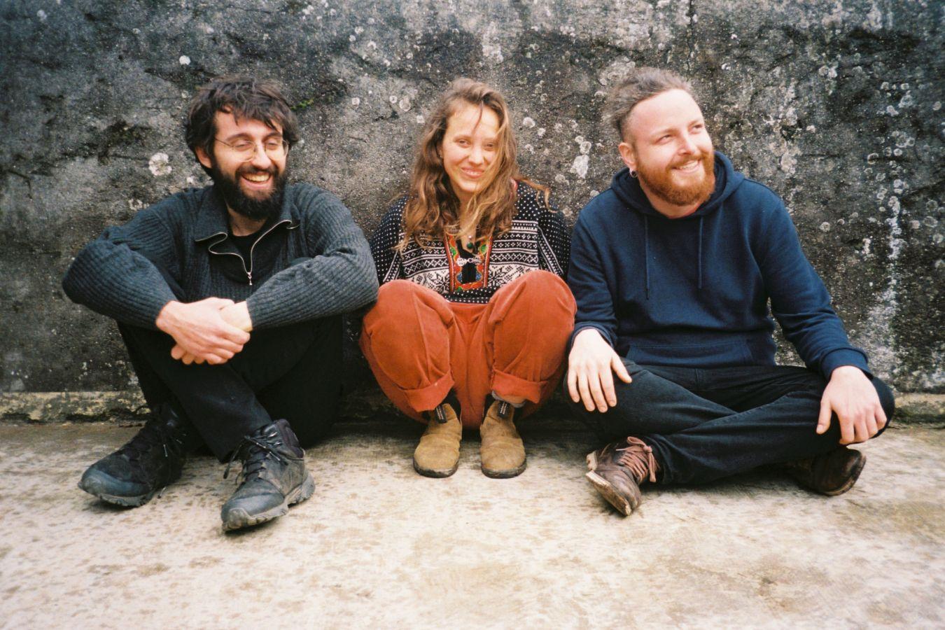 Die Mitglieder des Trios OTTO Gabriel Valtchev, Pol Small und Camille Émaille sitzen auf dem Boden und lachen in die Kamera.
