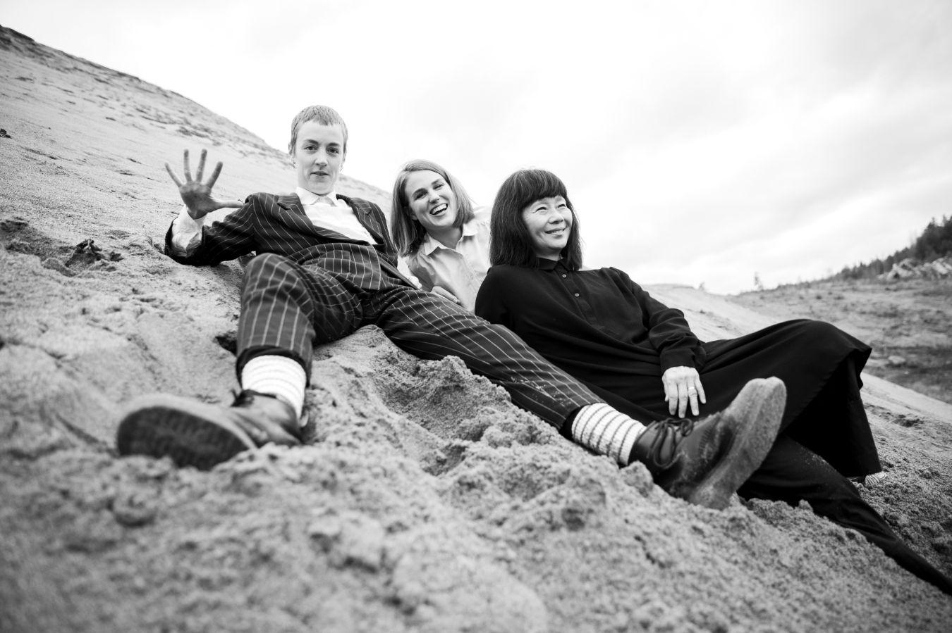 Lisa Ullén, Elsa Bergman und Anna Lund liegen lachend an einem sandigen Hang.
