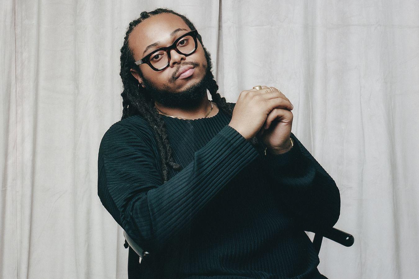 Portrait of Immanuel Wilkins sitting on a chair with his hands folded.
