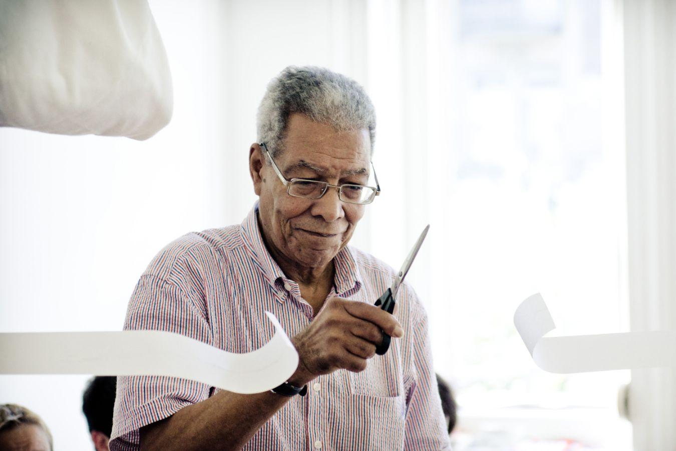 Der Fluxuskünstler Benjamin Patterson zerschneidet mit der Schere Papierstreifen.