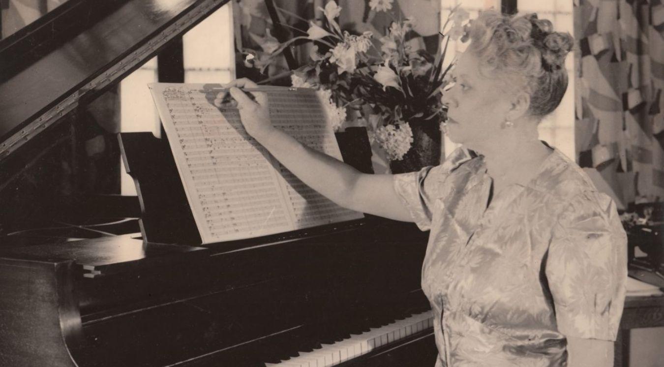 Florence Price sits at the piano at an advanced age, a score in front of her.