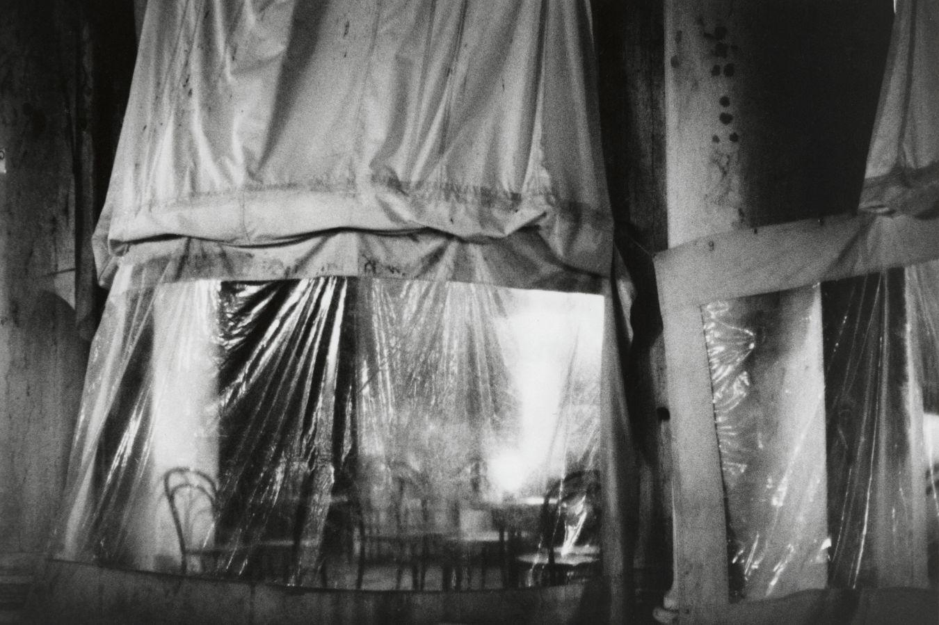 Chairs and tables of a café shimmer through a tarpaulin