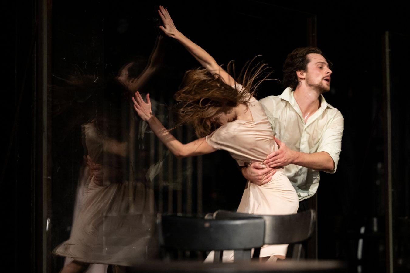 One male and one female dancer are in dynamic movement in front of a revolving glass door.