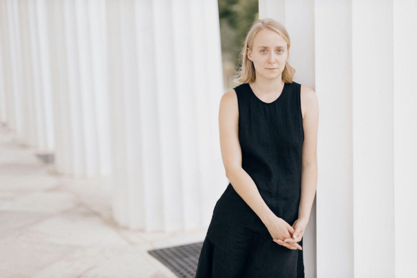 A woman in a black dress stands in front of white columns.