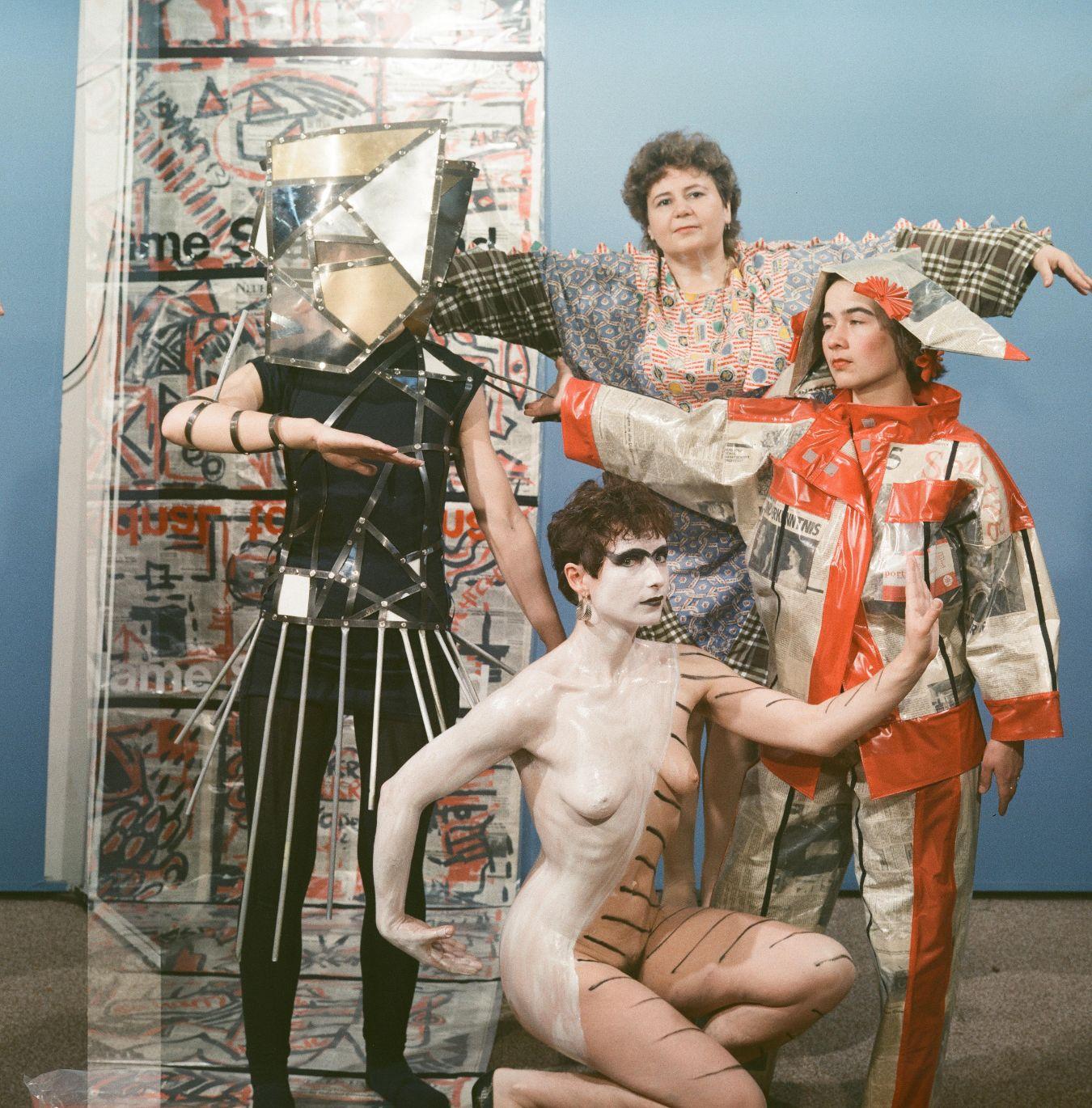 Gruppe von Personen in avantgardistischer Kleidung, darunter Metallmaske, bemalter Körper und Patchwork-Muster.