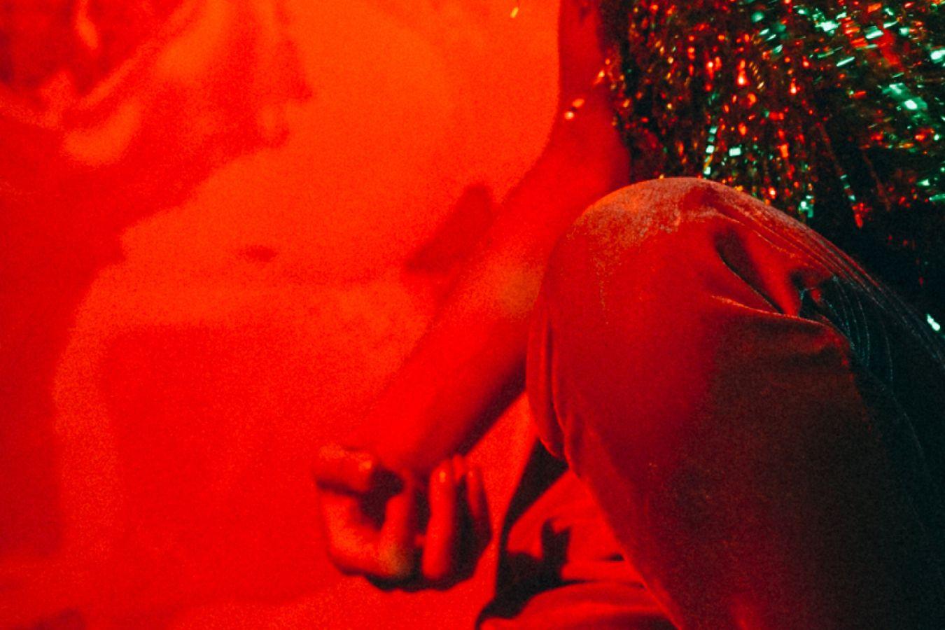 Knie und Hand einer Frau mit Glitzerperücke vor orangem Hintergrund