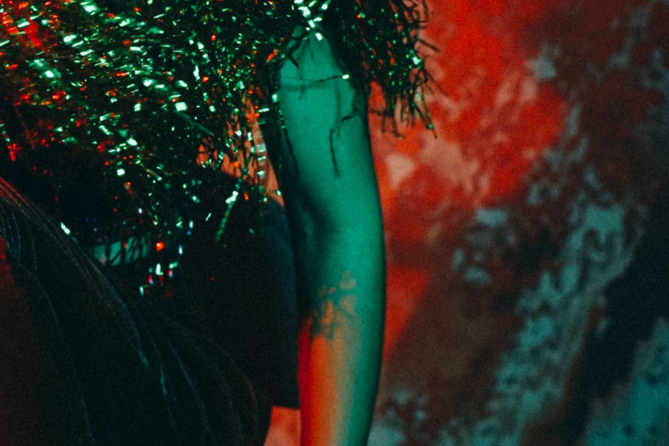Arm einer Frau mit Glitzerperücke vor orangem Hintergrund