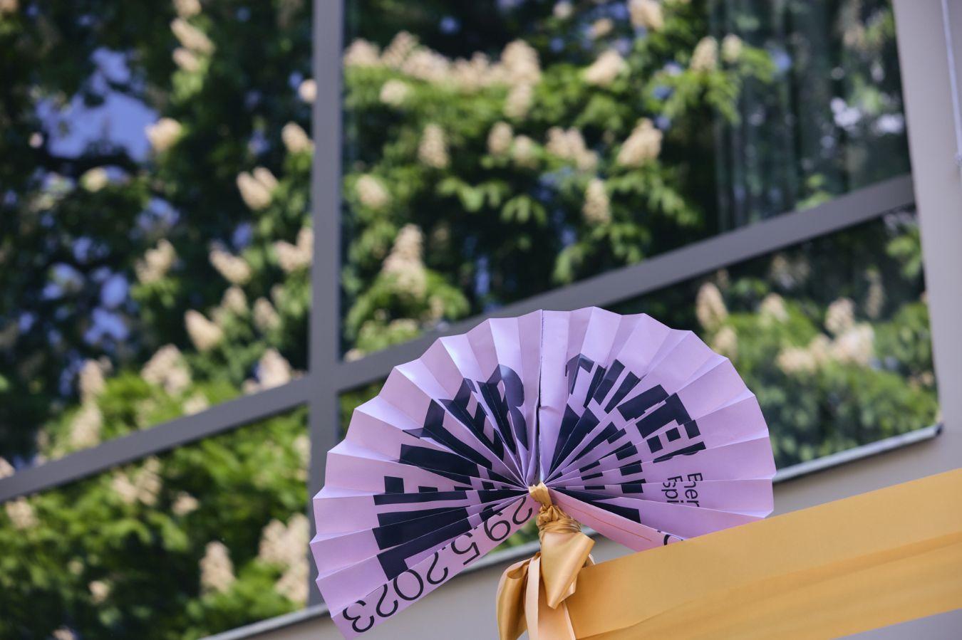 A purple fan bearing the word “Theatertreffen” sits in front of a large window, which reflects a blooming chestnut tree.