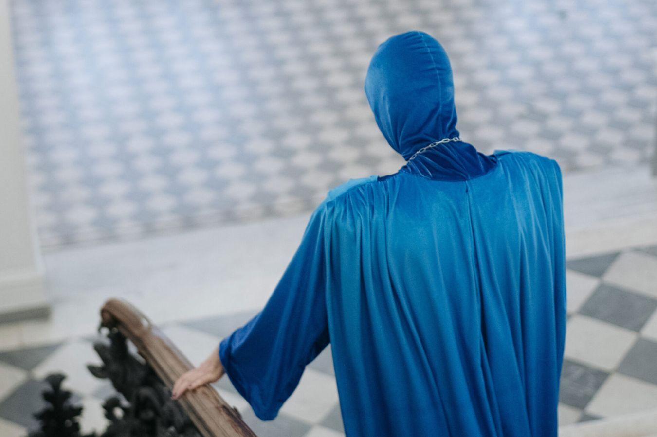 Eine Person in einem nachtblauen Umgang mit Kapuze geht eine Treppe hinunter.