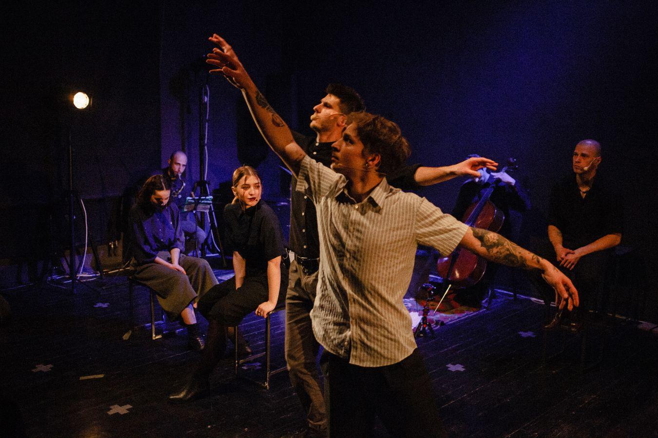 Zwei Personen tanzen, während sich mehrere Personen im Hintergrund befinden – sitzend, stehend oder musizierend.