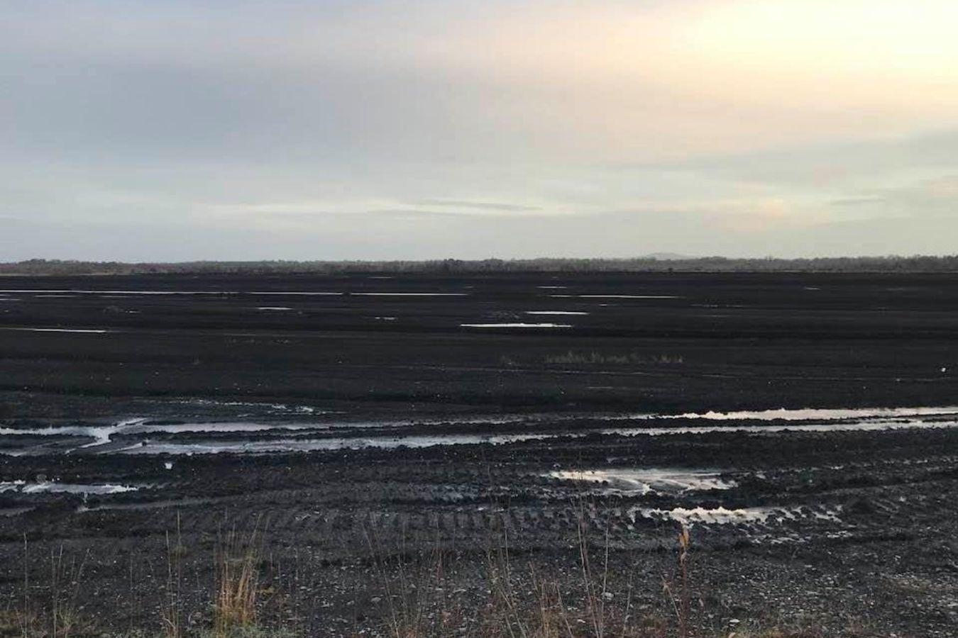 The traces of machines can be seen on a flat earthen landscape with a few puddles.
