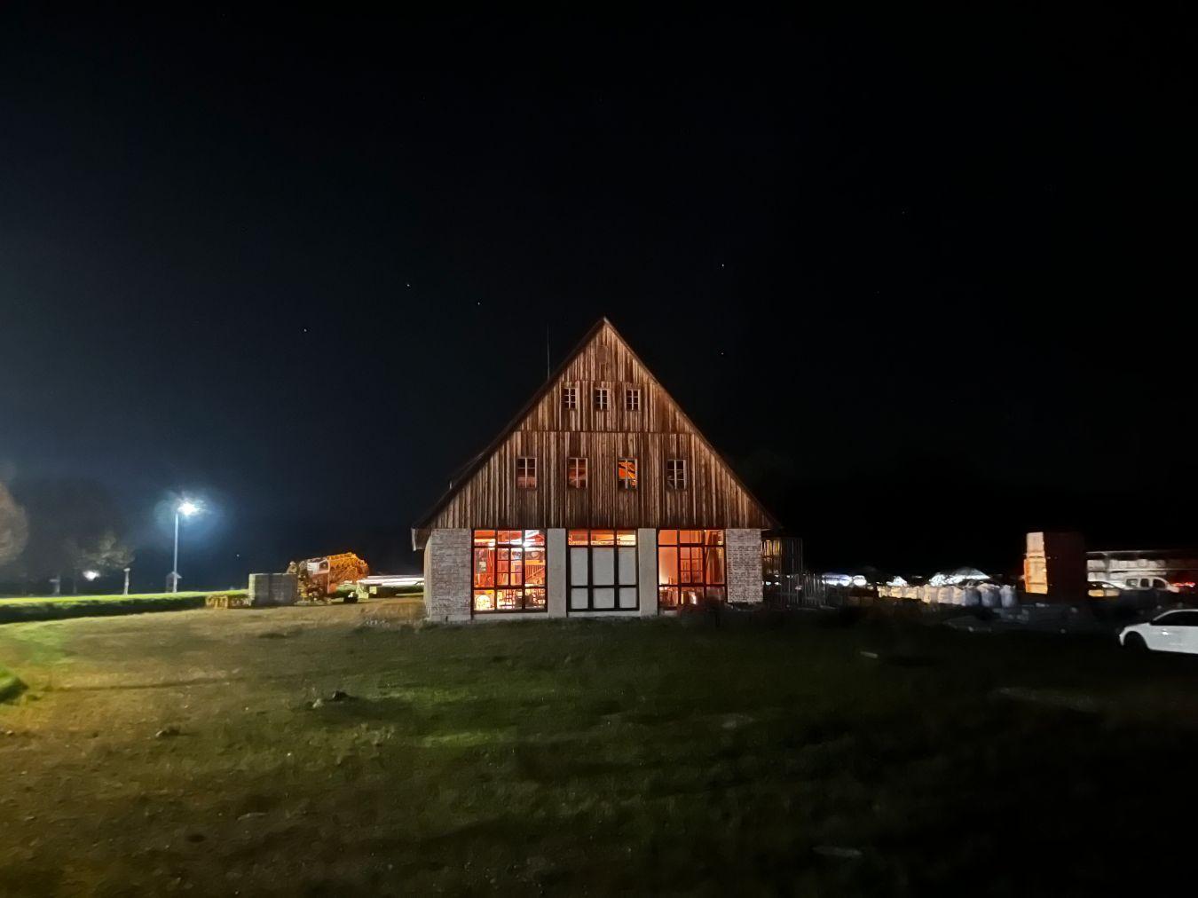 A brightly lit large barn in the middle of a meadow