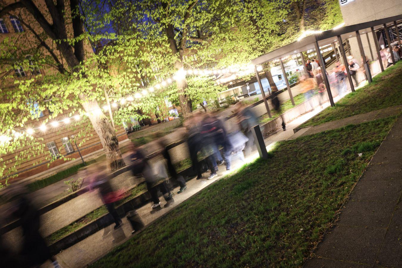 Blurred photo of a group of people in motion, in the evening on a path with a string of lights under trees.