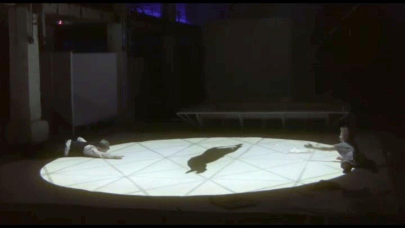 A circle of light on a stage in which two people stretch out their hands to the left and right