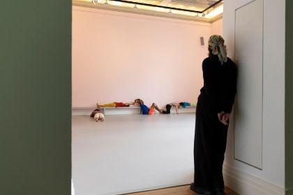 In a light pink-painted room, a live performance titled “study now steady” is taking place. Several dancers move dynamically through the space, incorporating the floor, walls, and benches into their choreography. A person is framed by the doorway, quietly observing.