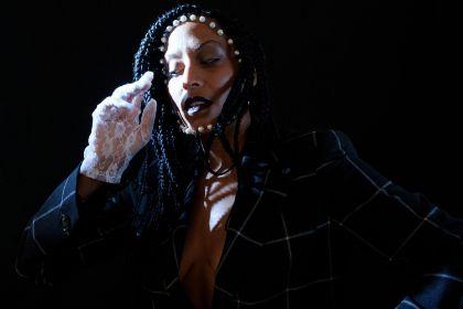 A person in motion raises a hand in lace gloves in front of their face, illuminated by a spotlight.